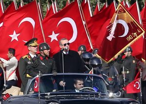 Turkish President Recep Tayyip Erdogan (R) speaks through a microphone next to Chief of the General Staff of the Turkish Armed Forces Hulusi Akar (L) as they are driven in a car past Turkish soldiers during a ceremony marking the 92nd anniversary of Republic Day on October 29, 2015 at the Ataturk Cultural Center in Ankara. AFP PHOTO / ADEM ALTAN