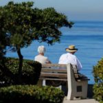 An elderly couple looks out at the ocean as they sit on a park bench in La Jolla, California